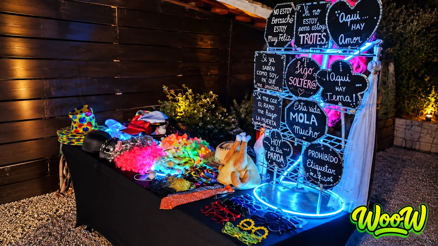 Mesa de atrezzo con carteles de frases y luces de neón junto al fotomatón en un evento de noche