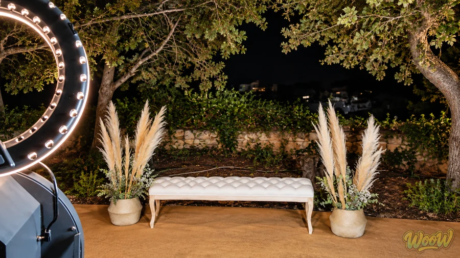 Rinc&oacute;n de fotomat&oacute;n con banco tapizado y pampa montado al aire libre en una boda de noche