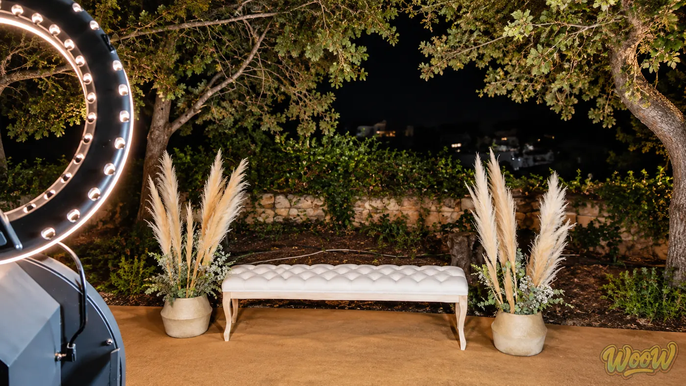 Rincón de fotomatón con banco tapizado y pampa montado al aire libre en una boda de noche