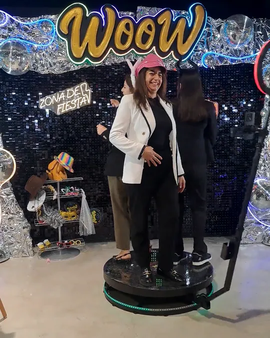 Dos invitadas saludando sobre la plataforma 360 de WooW delante del photocall de lentejuelas